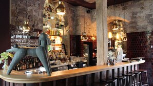 A bar with a rustic stone wall, shelves with bottles, and hanging pendant lights. - Renthof Kassel (Kassel)