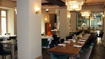 A restaurant with a long wooden table, green upholstered chairs, and hanging crystal chandeliers.