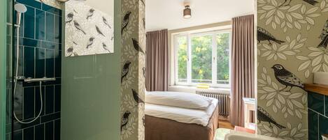 Un baño con ducha, cama y ventana con cortinas.