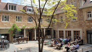 A courtyard with outdoor seating, stone buildings, and a tree. - Renthof Kassel (Kassel)