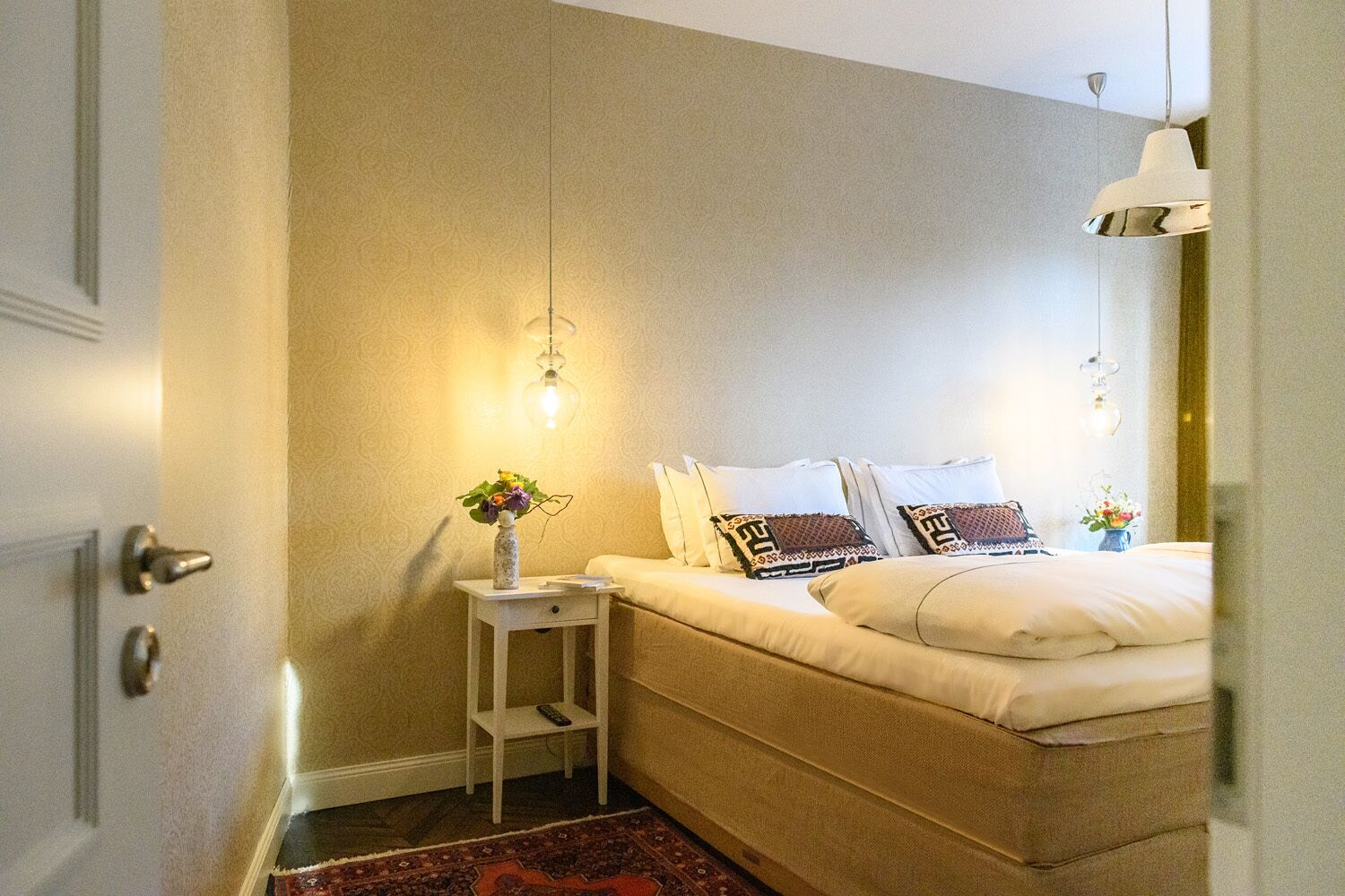 Un dormitorio con cama, mesita de noche y lámpara colgante.