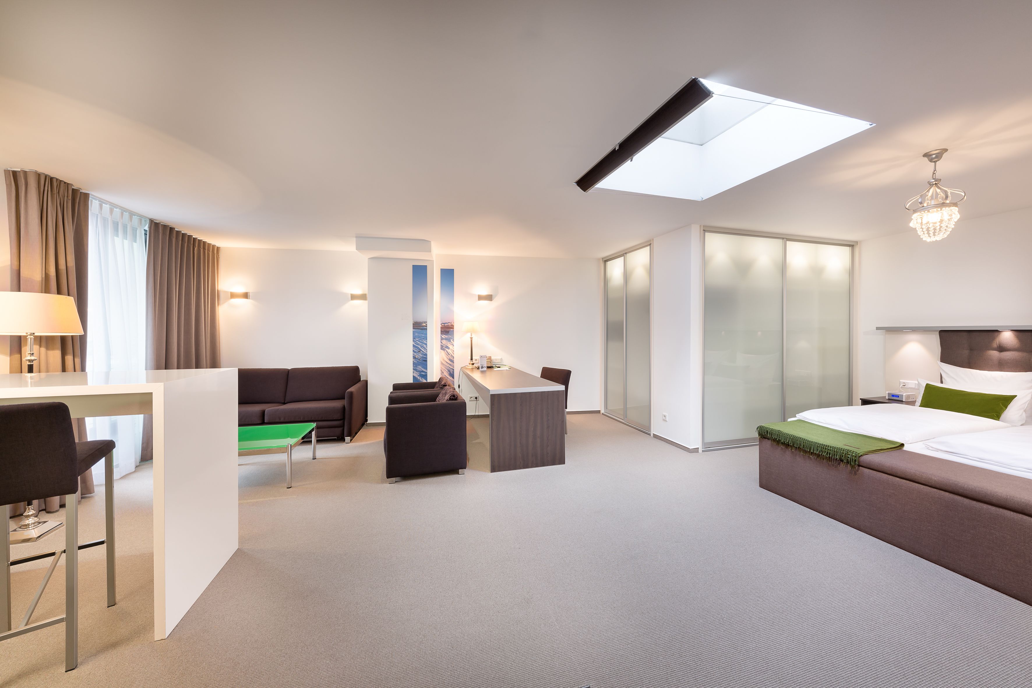 A modern hotel room with a bed, a desk, a sofa, and a dining area.
