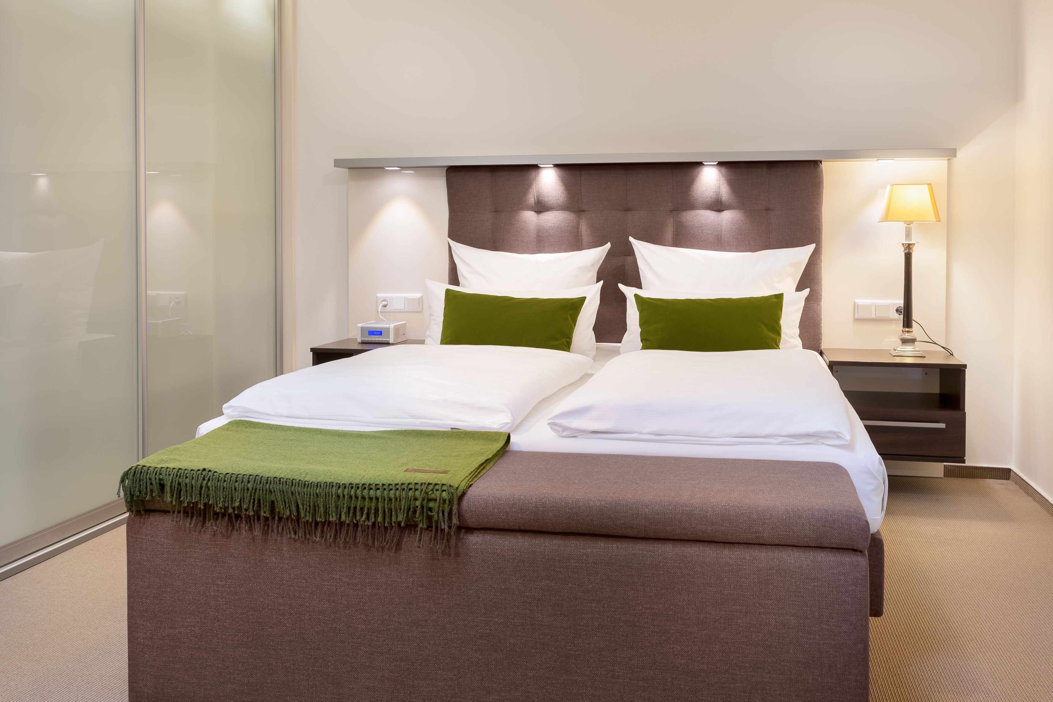 A hotel room with a bed, a nightstand, a lamp, and a wall-mounted control panel.