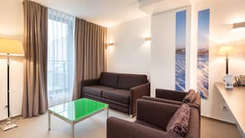 Una habitación de hotel moderna con sofá, sillones, una mesa de vidrio y un escritorio con lámpara.