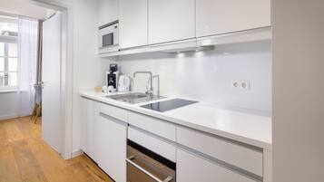 A modern kitchen with white cabinetry, stainless steel appliances, and a wooden floor.