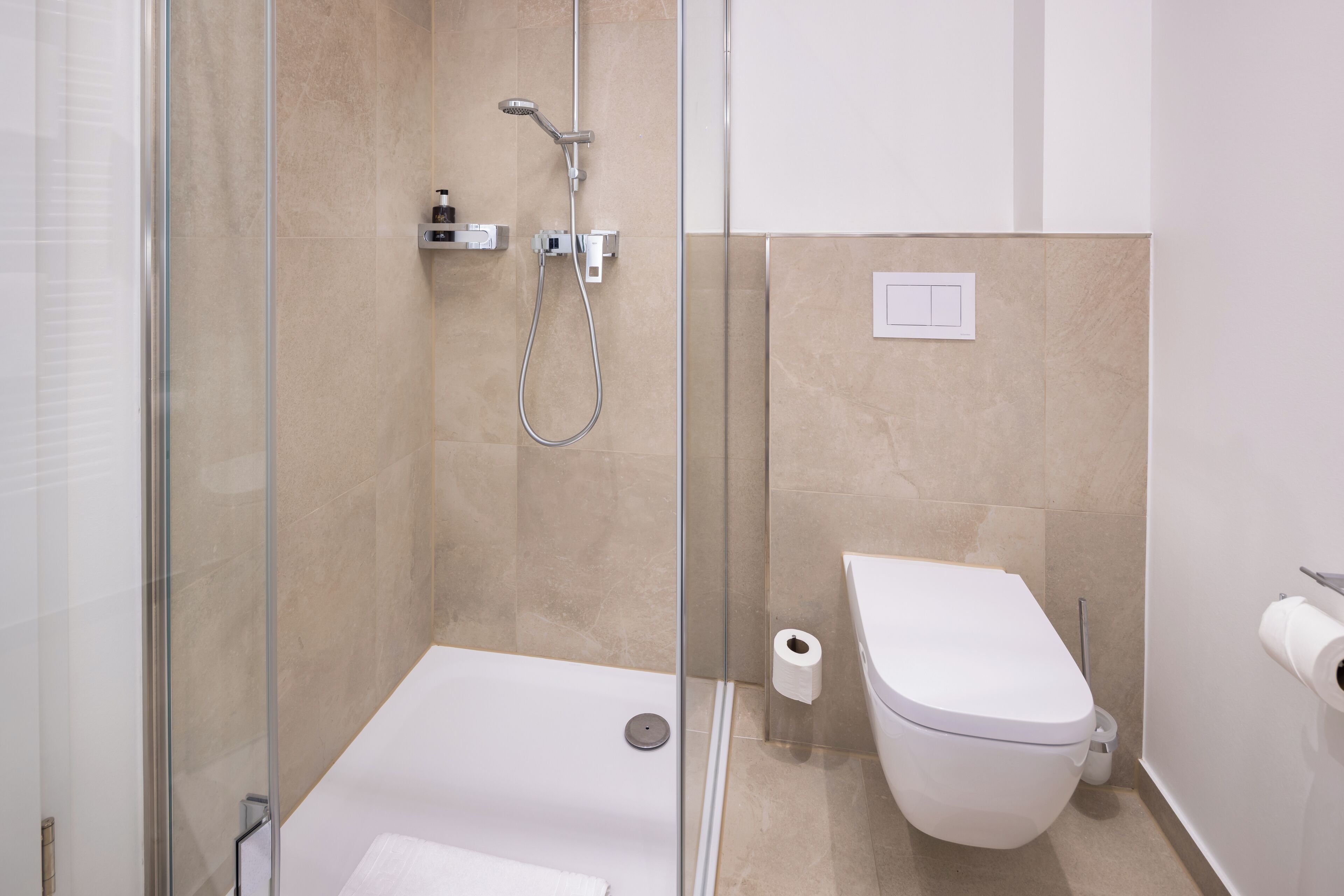 A modern bathroom with a glass-enclosed shower, a white toilet, and a visible toilet paper roll.