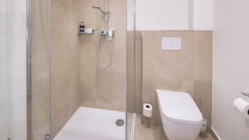 A modern bathroom with a glass-enclosed shower, a white toilet, and a visible toilet paper roll.