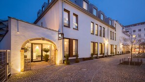 Een modern hotel met een geplaveide binnentuin, grote ramen en een goed verlichte ingang.