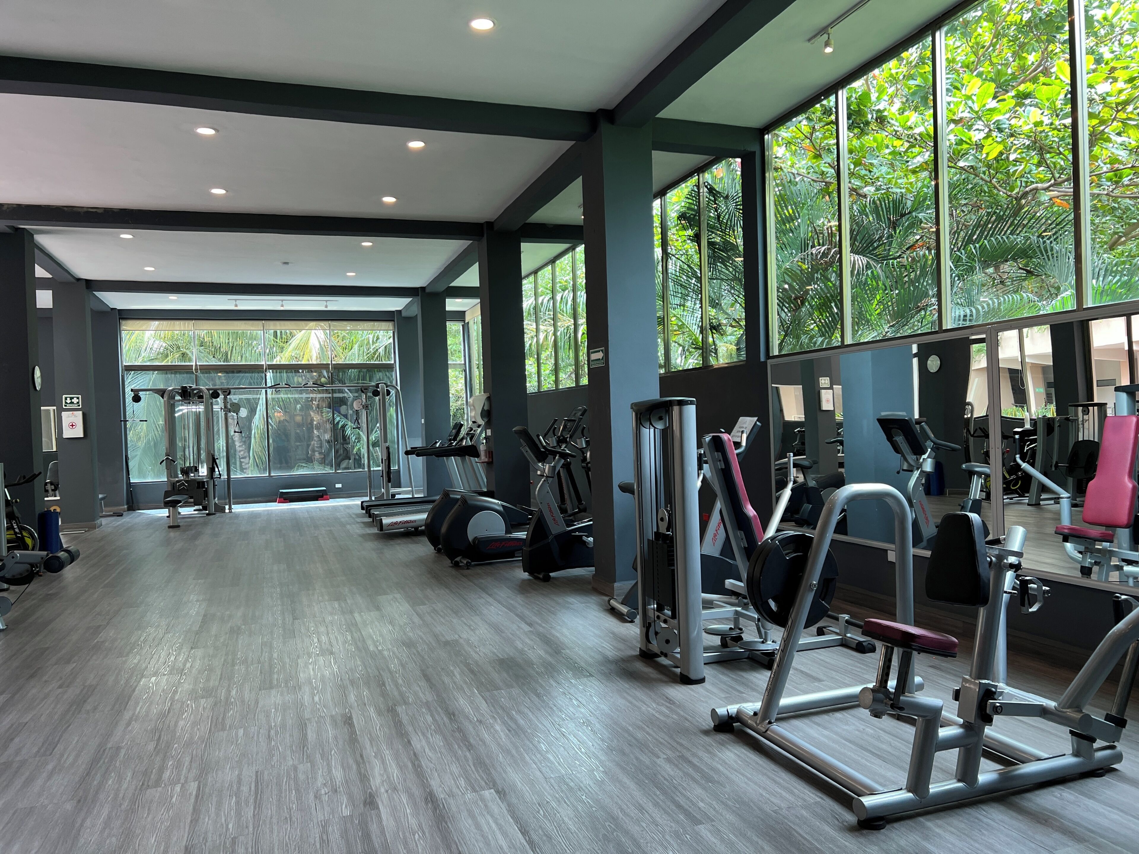 Ein Fitnessraum mit Trainingsgeräten, großen Fenstern und Holzboden.