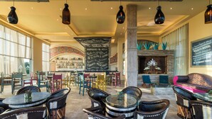 Un vestíbulo amplio con mesas y sillas redondas, una zona de bar y una chimenea.
