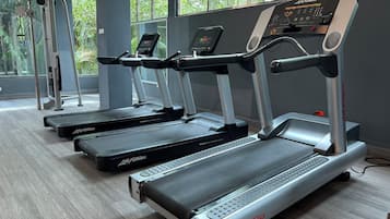 A row of treadmills with digital displays, a weight bench, and a window with a view of greenery.