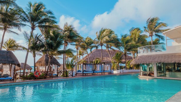 A swimming pool with thatched-roof structures and palm trees. - El Dorado Seaside Palms, All & More Inclusive - Adults Only - All inclusive (Kantenah)