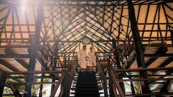 Una escalera de madera con estructura metálica, que lleva a una zona cubierta con vista a palmeras.