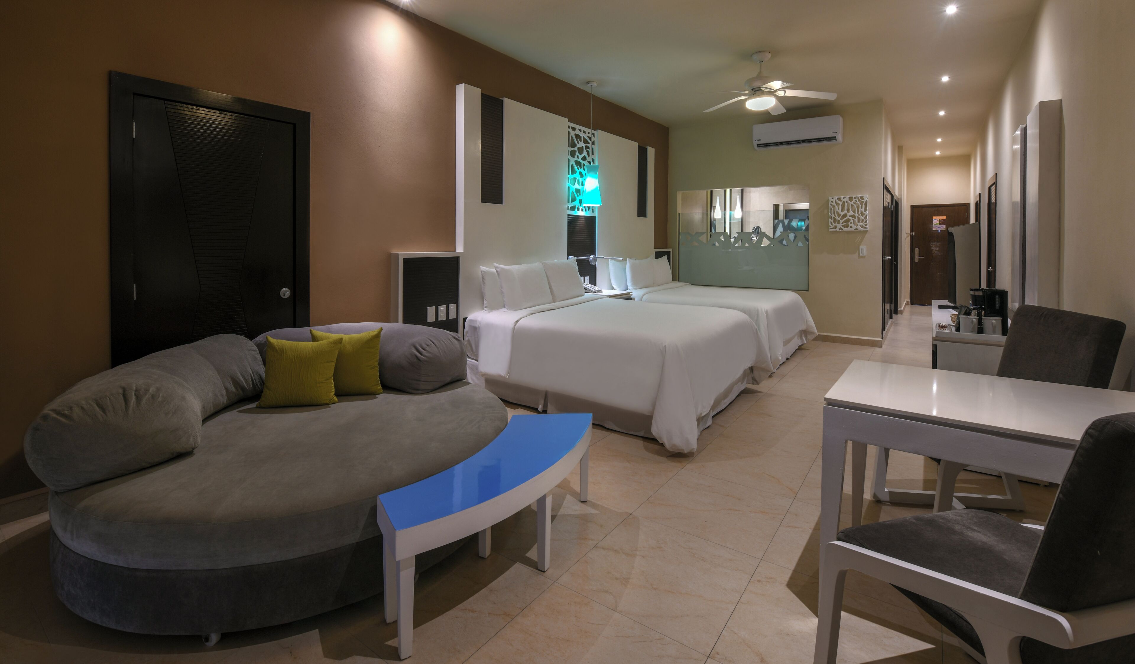 Une chambre d’hôtel avec un canapé incurvé, deux lits, un bureau et une chaise.