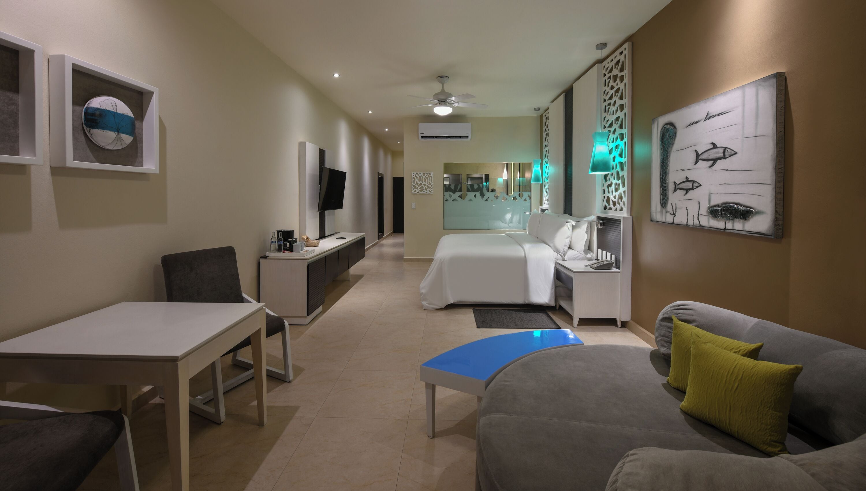 Une chambre d’hôtel équipée d’un lit, d’un canapé, d’un bureau, d’une télévision et décorée avec des œuvres d’art aux murs.