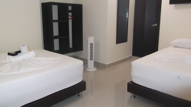 Habitación de hotel con dos camas, un armario, un televisor montado en la pared y un calentador portátil.