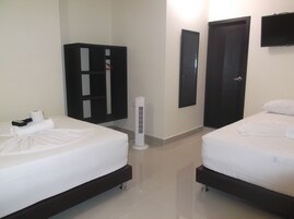Habitación de hotel con dos camas, un armario, un televisor montado en la pared y un calentador portátil.