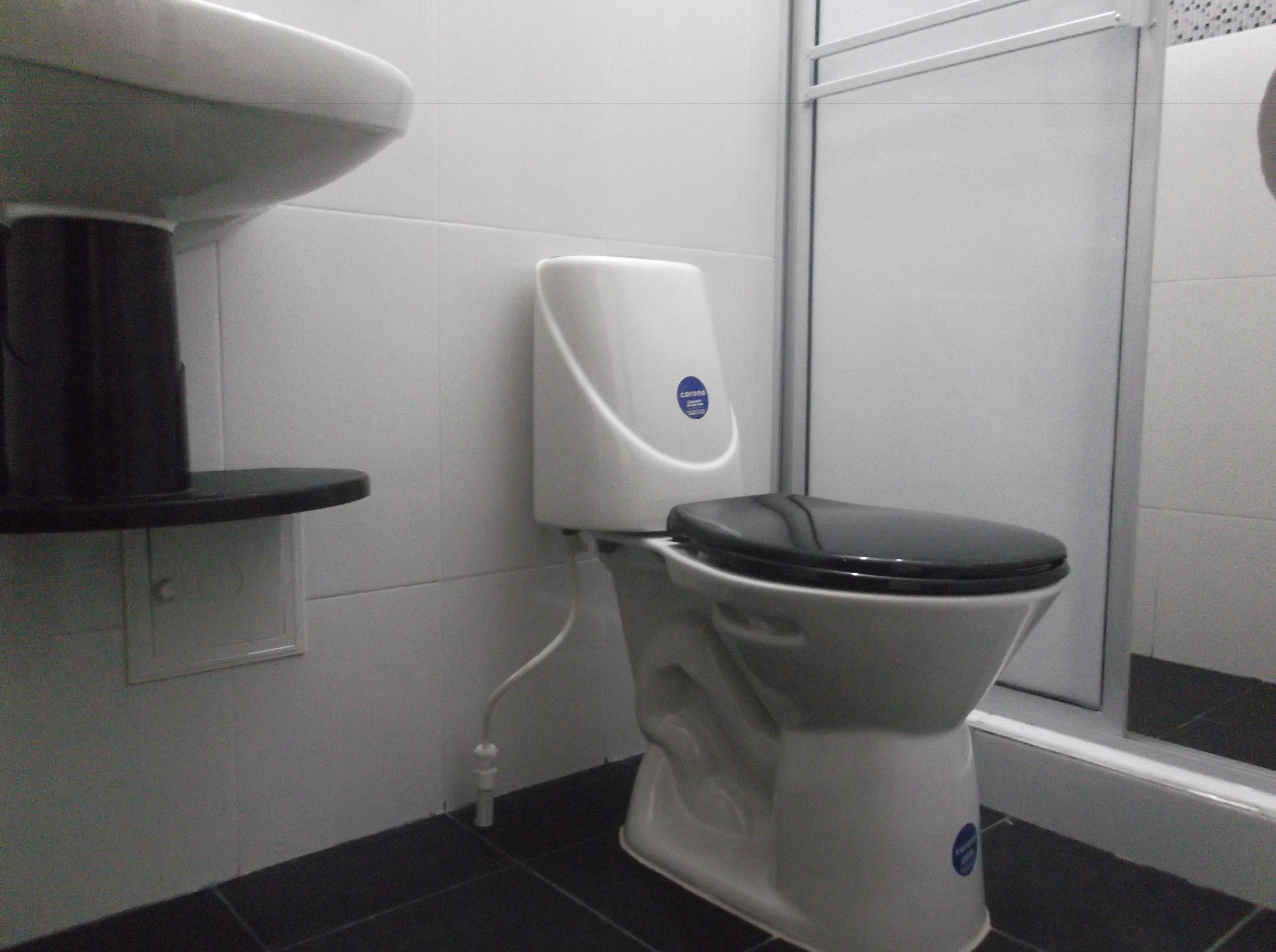 A modern bathroom with a toilet, a soap dispenser, and a black shelf.