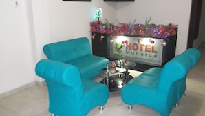 Un hall de hotel con sillones azul verdosos, una pequeña mesa redonda con un jarrón y velas, y un cartel que dice "HOTEL Monarca".