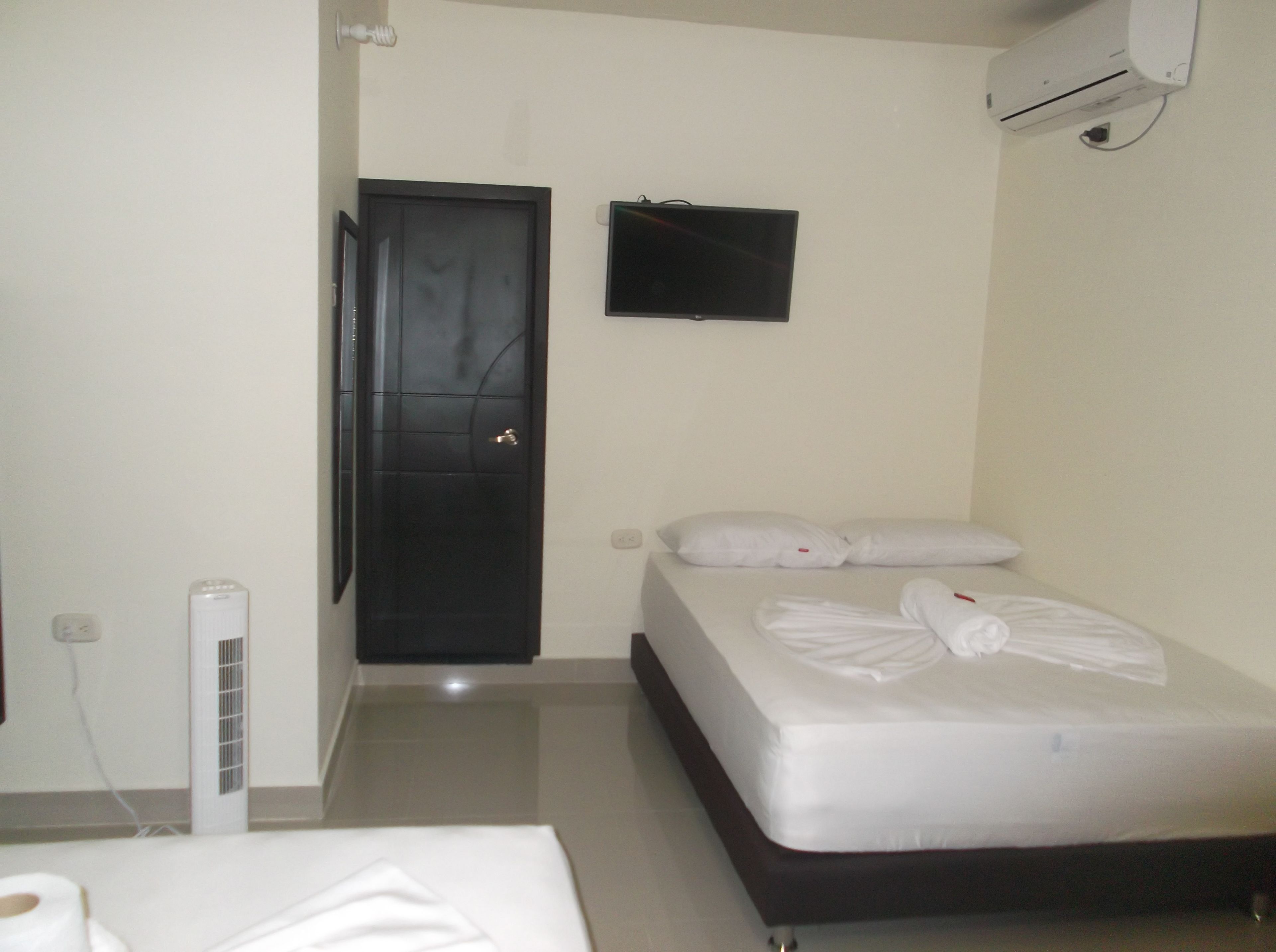 A hotel room with a bed, a wall-mounted TV, a door, and an air conditioning unit.
