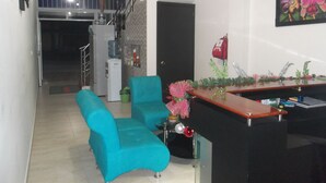 Una sala de estar moderna con sofás azul verdosos, una mesa de centro de madera y una zona de cocina con refrigerador y dispensador de agua.