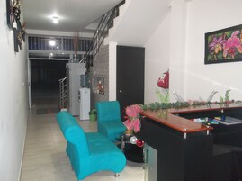 Una sala de estar moderna con sofás azul verdosos, una mesa de centro de madera y una zona de cocina con refrigerador y dispensador de agua.