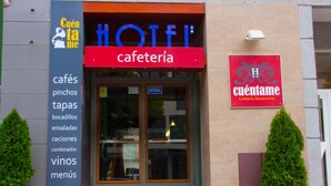 A hotel with a red sign reading "HOTEL" and "cafetería". There is a sign on the left listing food and drink options like "cafés", "pinchos", and "tapas". - Hotel Cuéntame (Burgos)