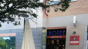 An outdoor seating area with red chairs and a table, a building with a 'HOTEL' sign, and a 'cuentame' sign indicating a restaurant. - Hotel Cuéntame (Burgos)