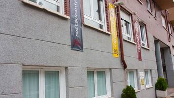 Een gebouw met veel ramen, waarvan sommige voorzien zijn van gordijnen, en verschillende banners die een restaurant en een café promoten.