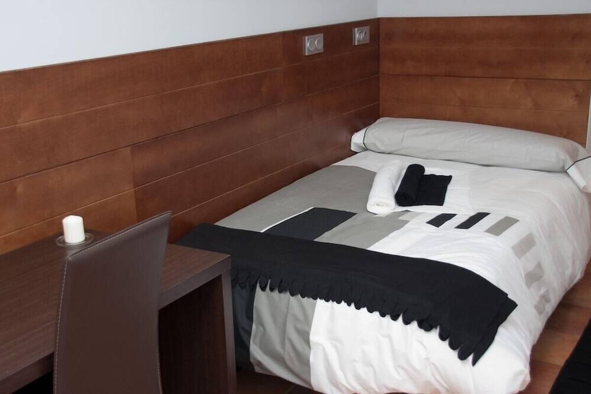 A single bed with a wooden headboard, a bedside table, and a small white candle.