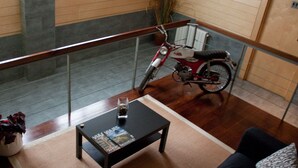 A living room with a wooden floor, a black coffee table with magazines, a red motorcycle, and a glass railing. - Hotel Cuéntame (Burgos)