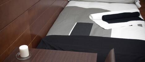 A neatly made bed with a pillow and a rolled towel, a bedside table with a white object, and a wooden headboard.