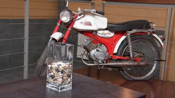 Una motocicleta con una combinación de colores blanco y rojo, un asiento visible y un espejo retrovisor, sobre una superficie oscura junto a un recipiente de vidrio transparente lleno de piedras.