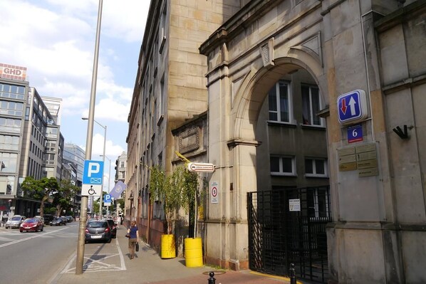 A street view with a building featuring an arched entrance, a blue parking sign, and a yellow barrel. - LoftHotel Przychodnia (Warsaw)