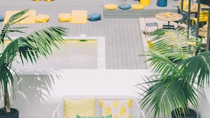 A person lying on a yellow bean bag chair using a laptop, with a white table and a patterned rug nearby.