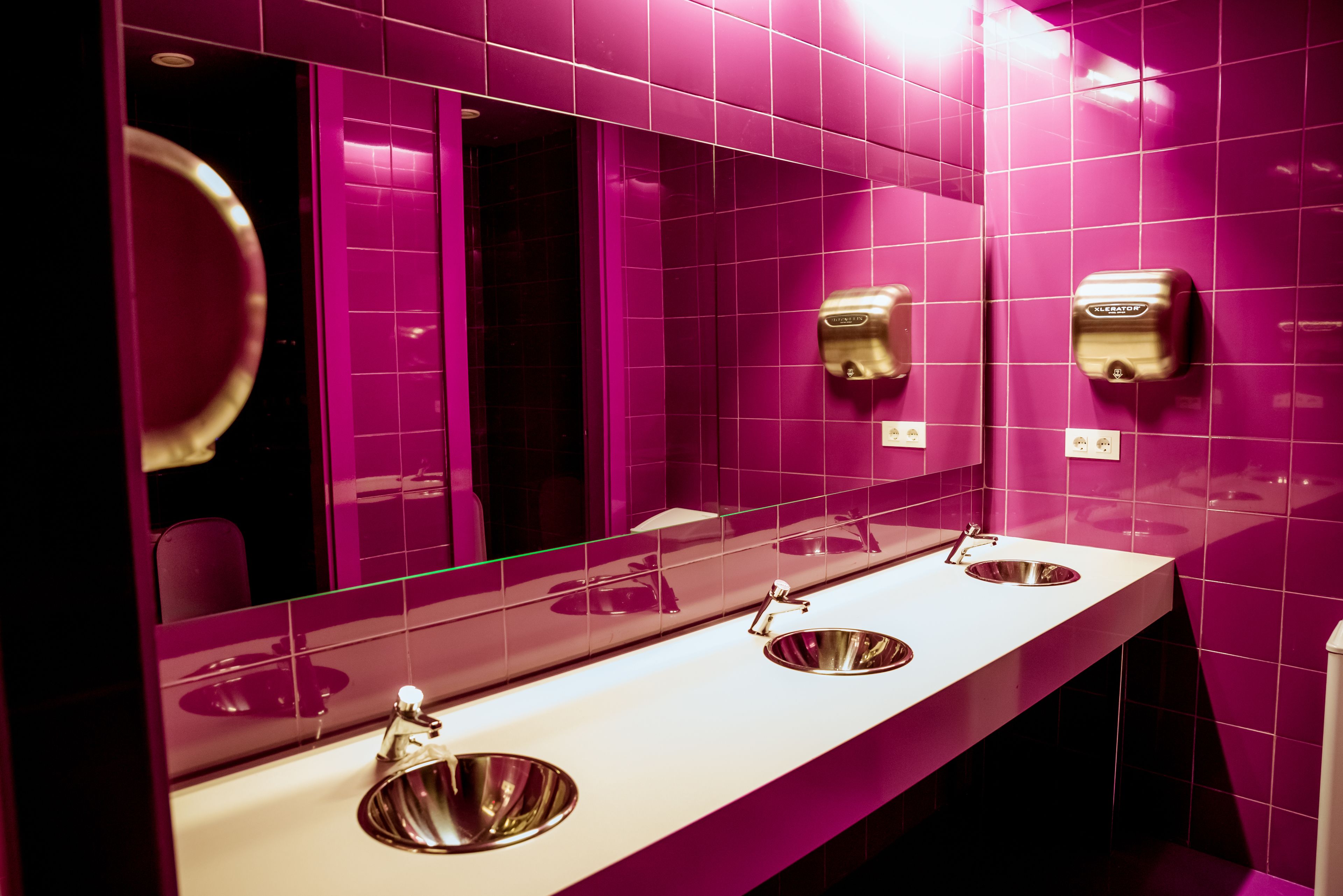 Baño con dos lavamanos, un espejo y un secamanos.
