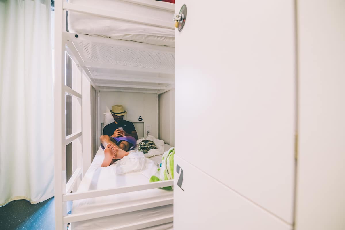 Une chambre avec un lit superposé, une fenêtre, un rideau et une personne allongée sur le lit.