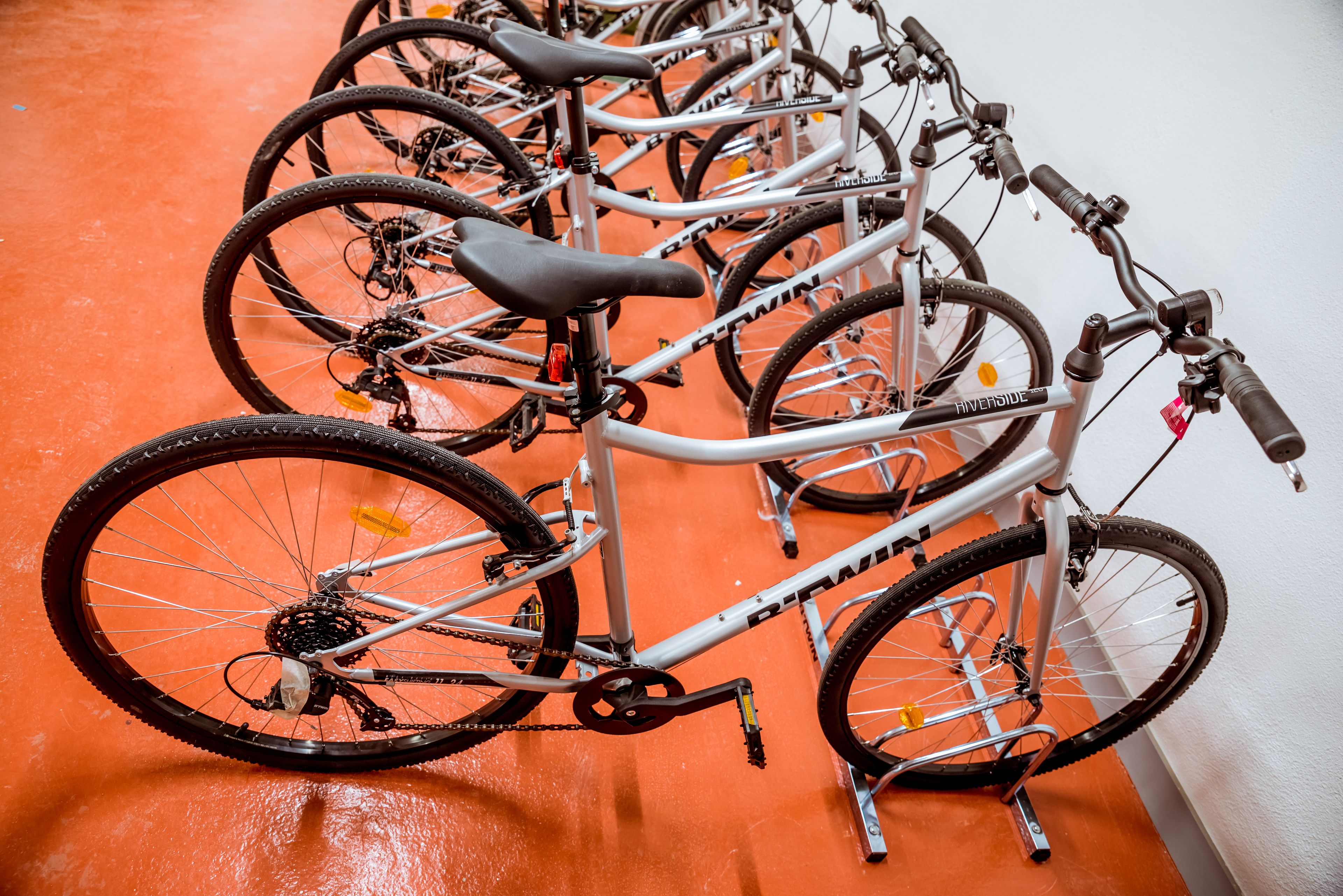 A row of bicycles parked indoors on an orange floor.