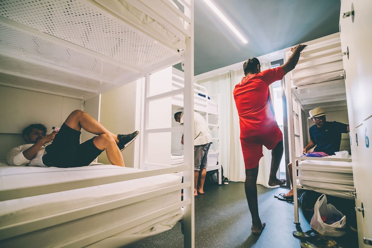 Une chambre avec un lit superposé, où une personne est allongée sur le lit du bas et une autre est en train de monter sur le lit du haut.