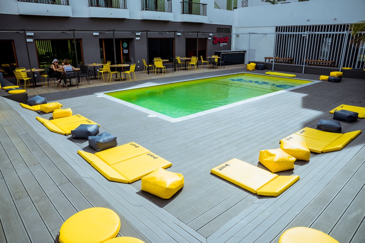 Un espace piscine sur le toit, avec des meubles de jardin jaune et gris, une piscine, ainsi que des tables et des chaises pour prendre les repas en plein air.