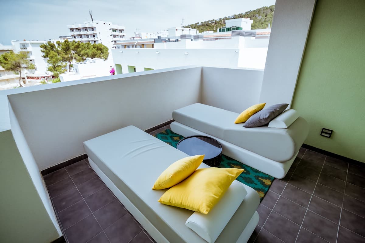 Un balcon avec deux canapés blancs, dont l’un est agrémenté de coussins jaunes et l’autre de coussins gris, et une petite table ronde.