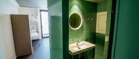Ett modernt badrum med ett vitt handfat, en rund spegel och gröna väggar.