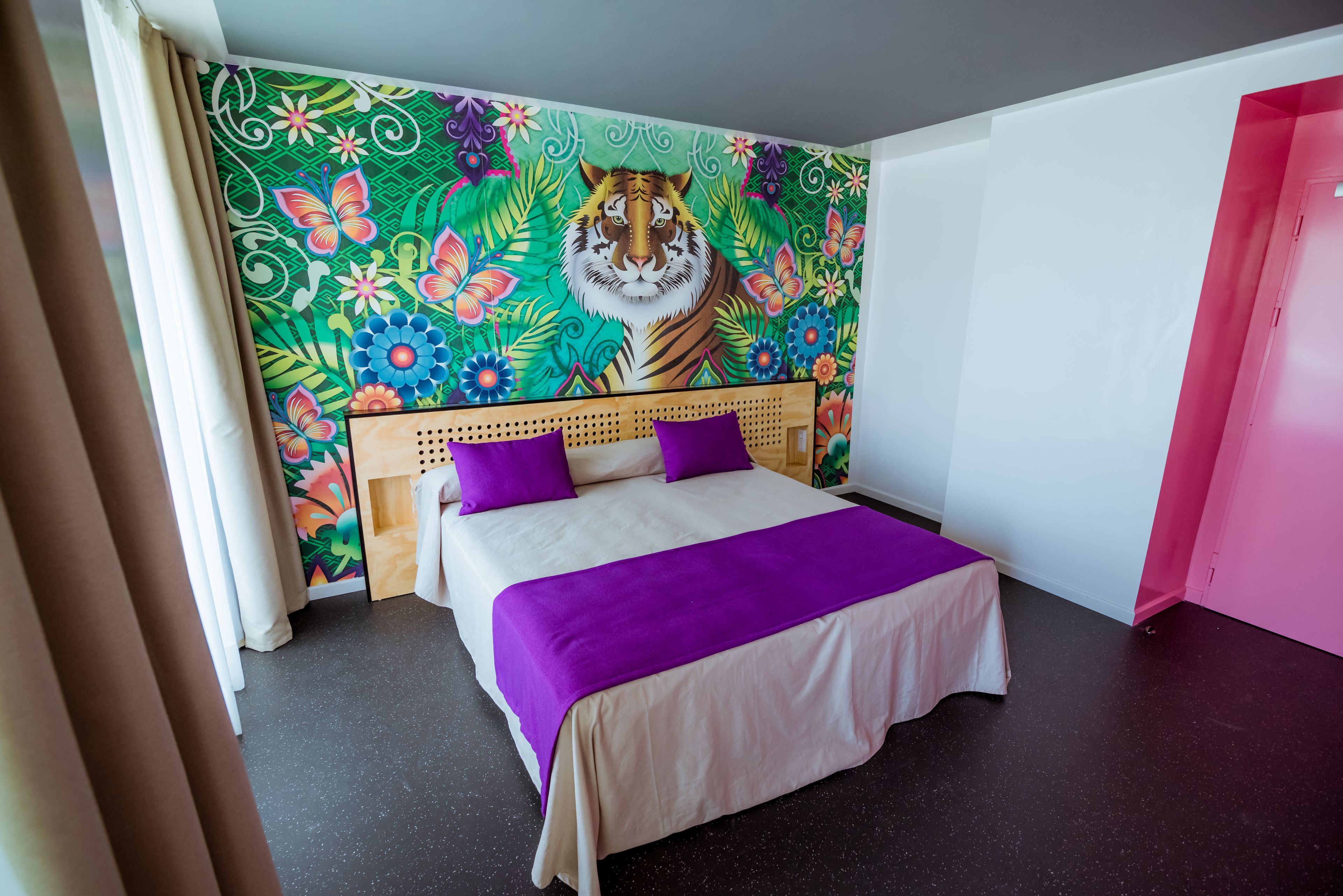 A bedroom with a bed, a headboard, and a colorful tapestry on the wall.