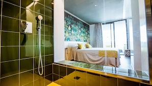 A modern bathroom with a shower, a bed with a headboard, and a large window.
