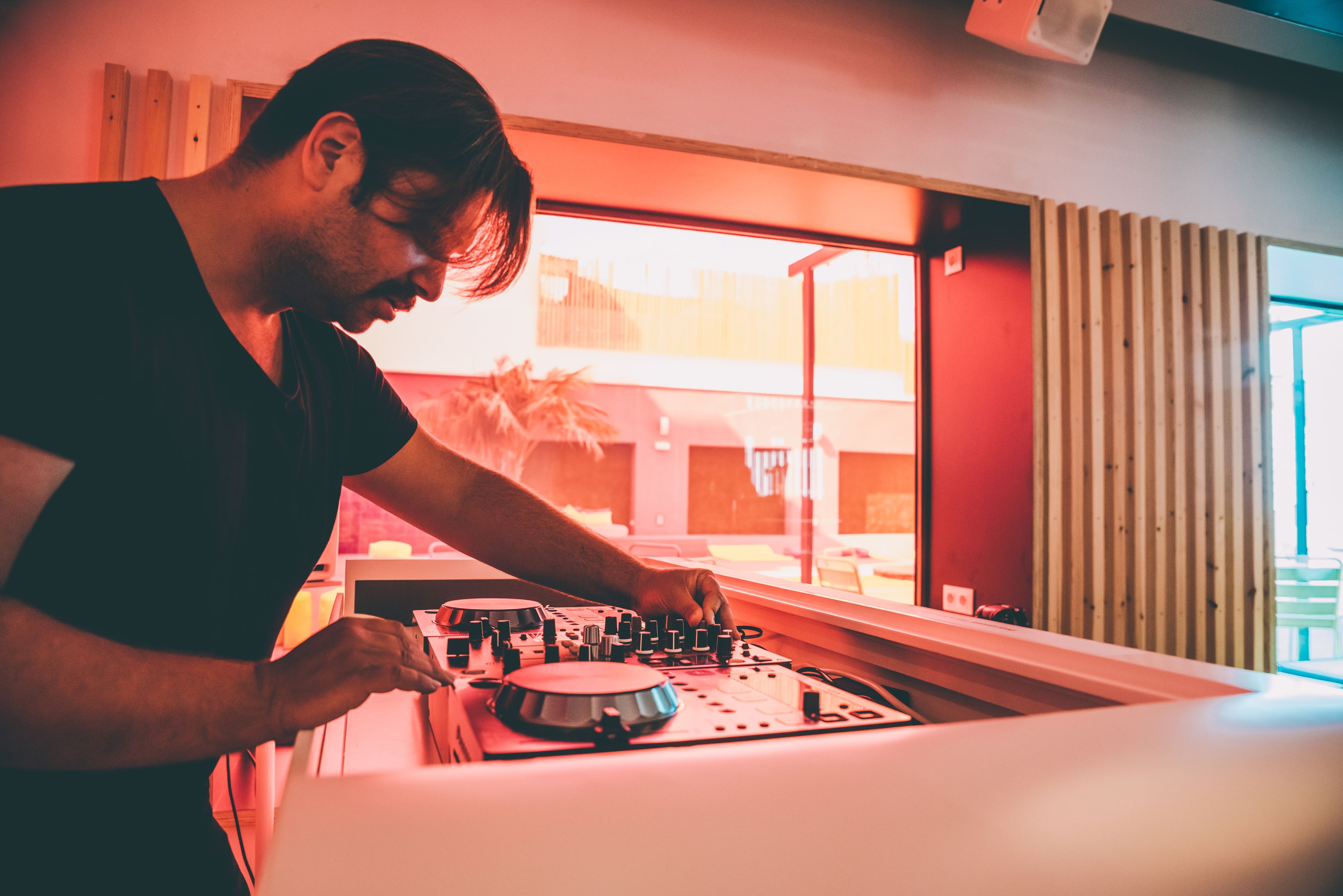 Una persona manejando equipo de DJ en una habitación con un ventanal grande y paneles de madera.
