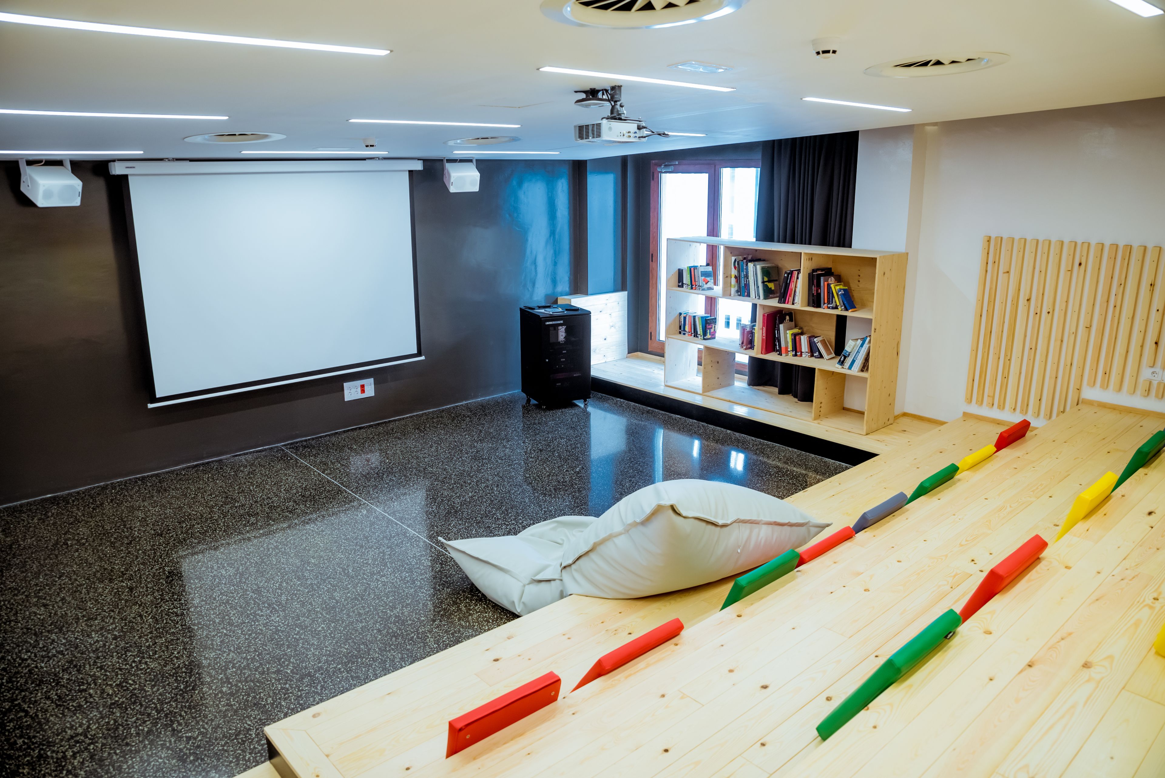 A modern conference room with a projector screen, a bookshelf, and a wooden table with colorful blocks.