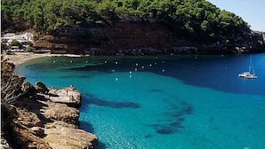 A coastal area with clear blue water, rocky cliffs, and a sailboat.