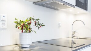 A modern kitchen with a stainless steel countertop, a white vase with red chili peppers, and a built-in microwave above the sink. - Biz Apartment Hammarby Sjostad (Stockholm)