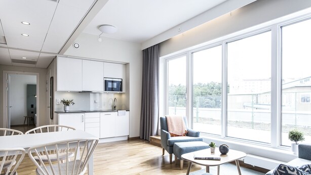 A modern living room with a dining area, large windows, and a kitchen in the background. - Biz Apartment Hammarby Sjostad (Stockholm)