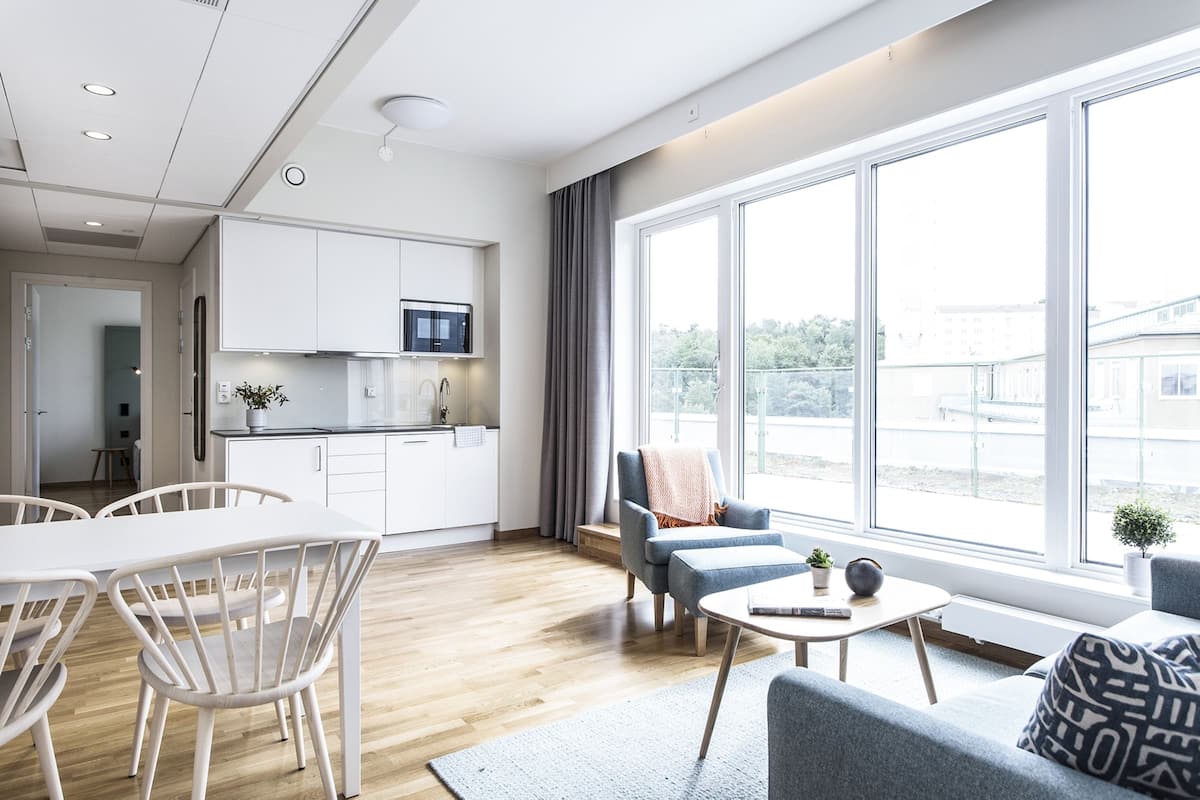 Een moderne woonkamer met een eethoek, grote ramen en een keuken op de achtergrond.